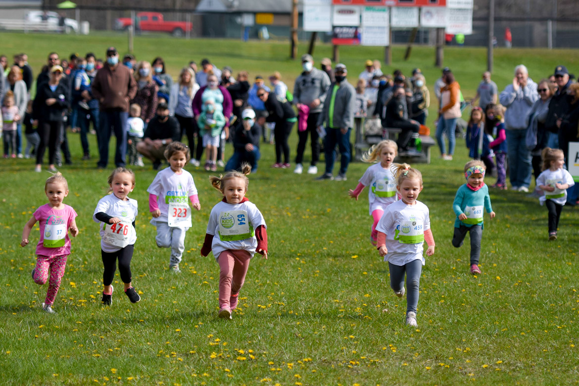 Kids run towards the finish line of a race as parents watch and cheer from behind them